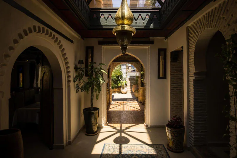 An arched corridor of the riad under a painted ceiling, lit by a brass lantern