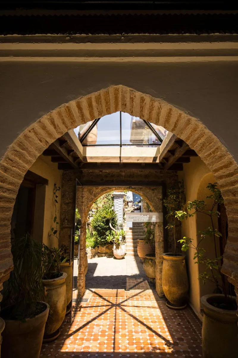 A brick arch framing a corridor that opens onto the garden, with potted plants on a tiled floor