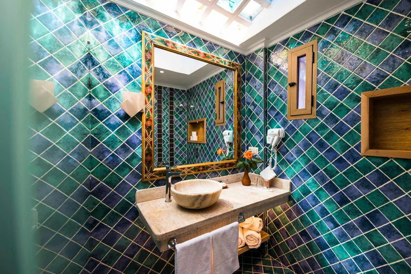 A wall of green zellij tiles behind a carved mirror and a stone basin