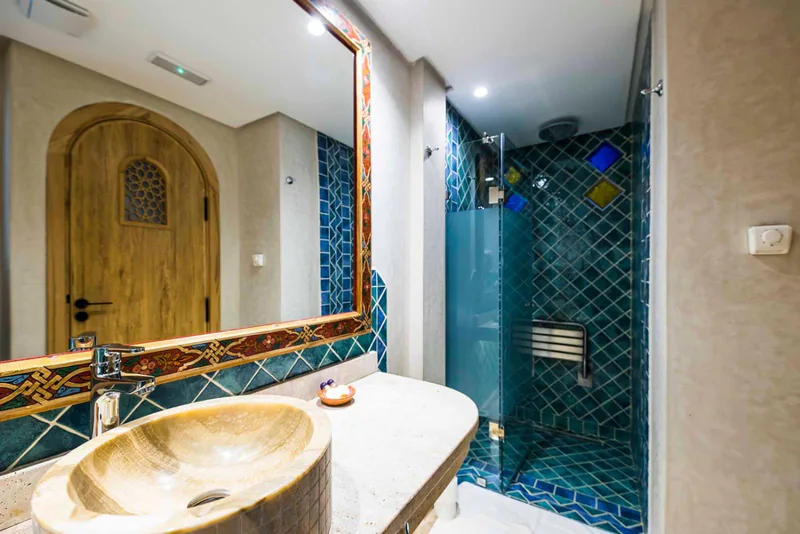 A bathroom with a stone basin, a framed mirror and a shower tiled in green zellij