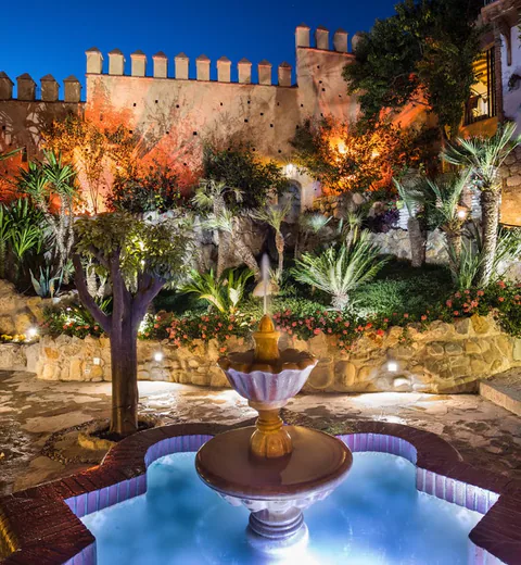The tiled fountain in the garden at night, running beneath the lit ramparts