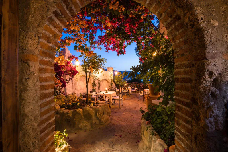 A brick arch hung with bougainvillea, opening onto the garden courtyard at dusk
