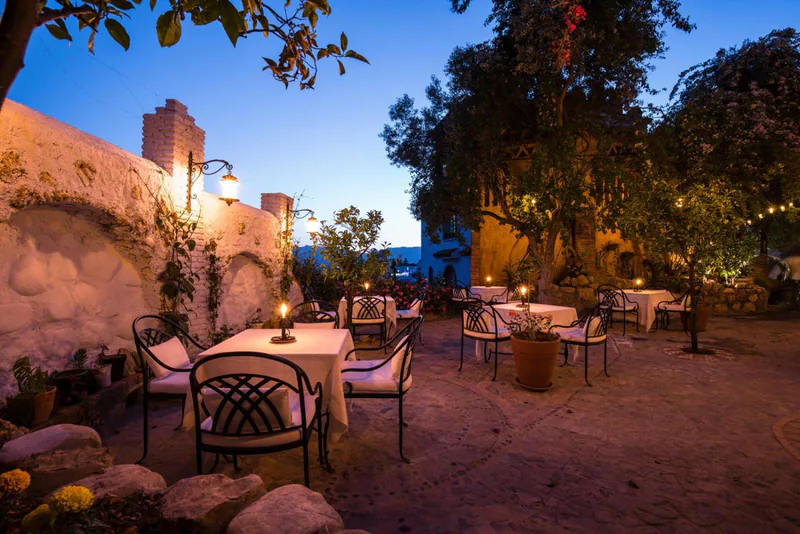 Tables set under the trees in the garden courtyard at dusk, lit by lanterns
