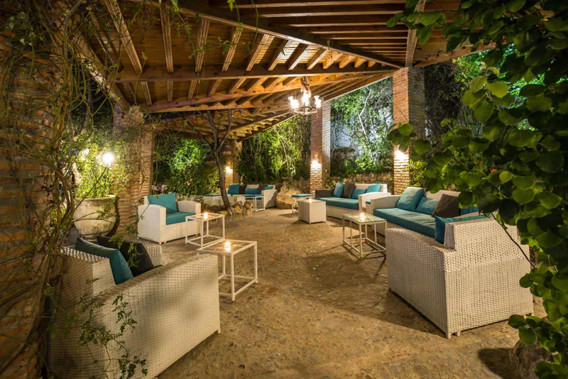 Wicker armchairs under a wooden pergola hung with greenery and lamps