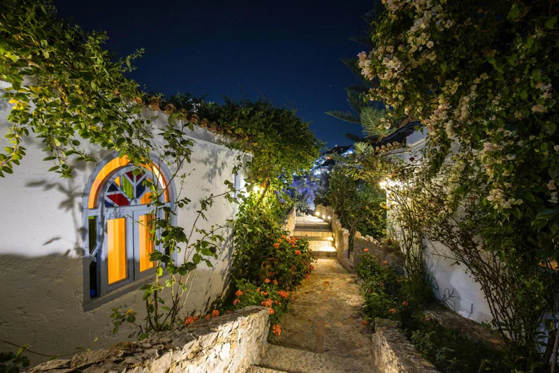A stained-glass window on a whitewashed wall, framed by climbing greenery and flowers