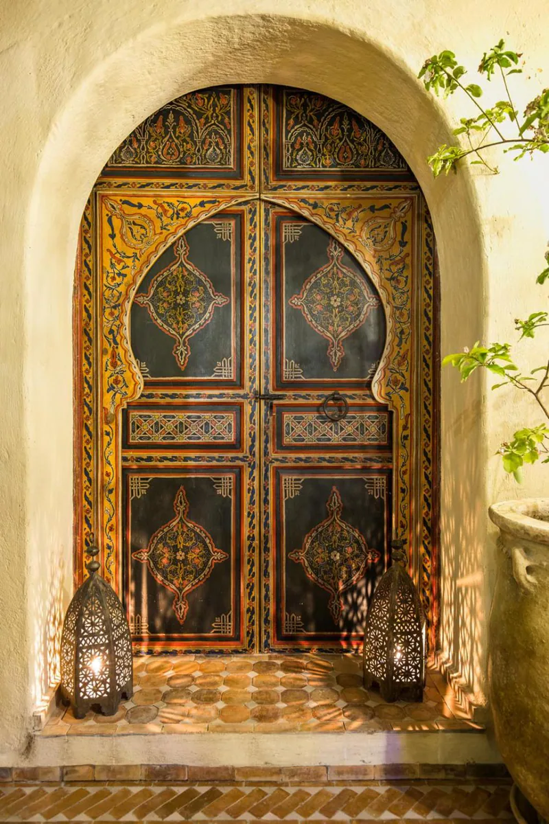 A carved and painted Moroccan door set in an arched doorway, with lanterns on the tiled floor