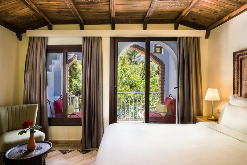 A room with its balcony doors open onto the garden and the hills