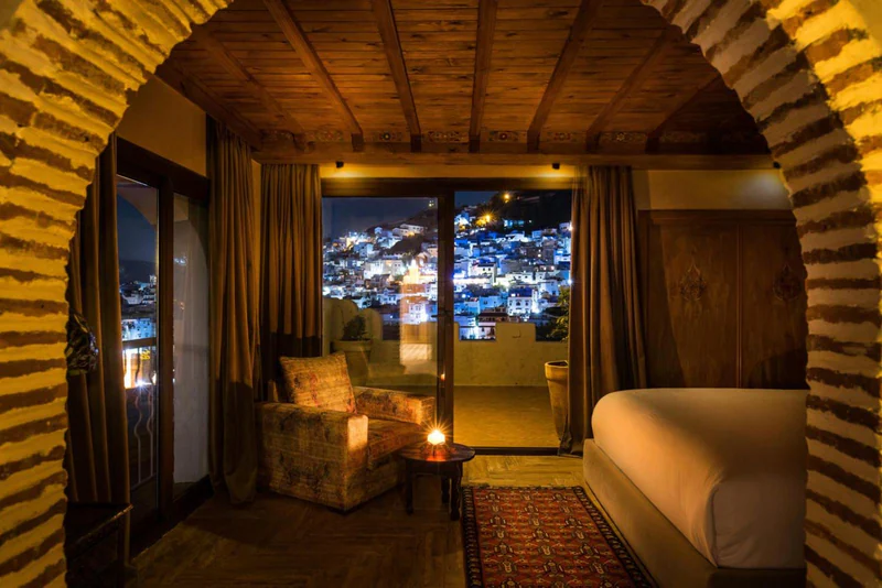 A room at night, its door open to a balcony above the lights of Chefchaouen