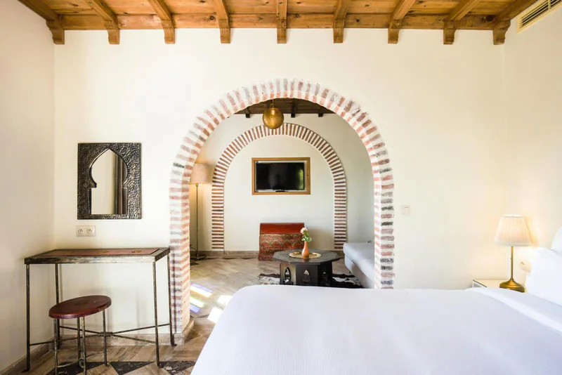 A grey corner sofa beneath a brick arch, with the bed beyond