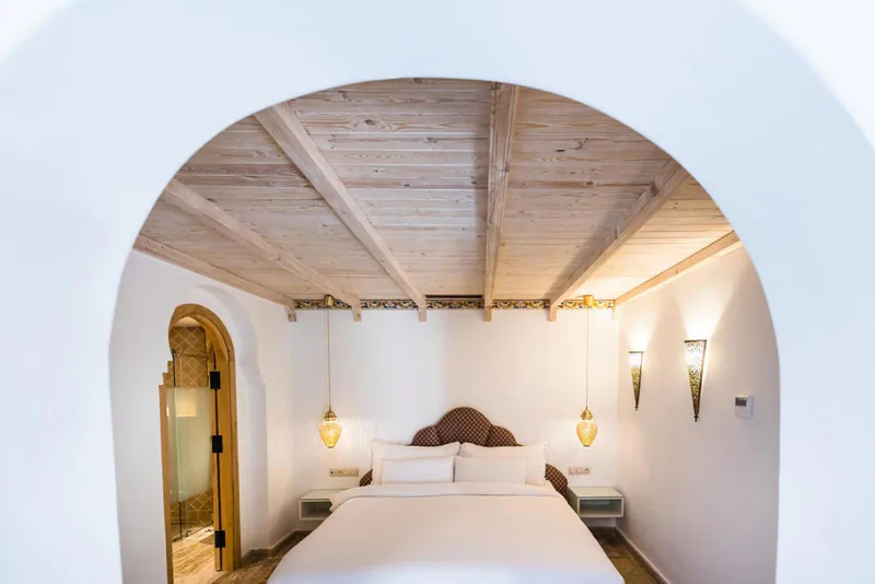 A white room under a wooden ceiling, with two hanging lanterns beside the bed