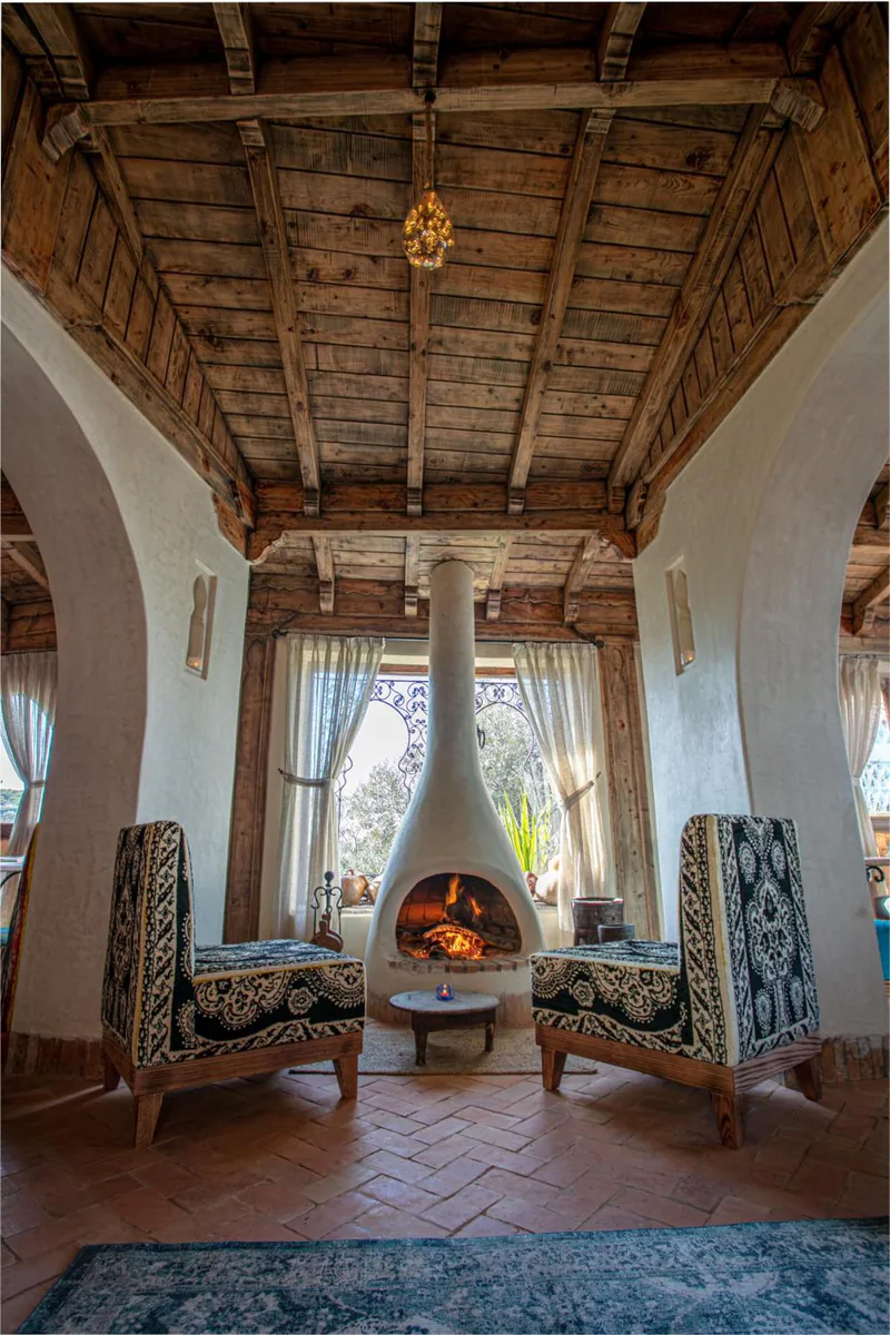 A salon with a domed fireplace, patterned armchairs and a wooden ceiling