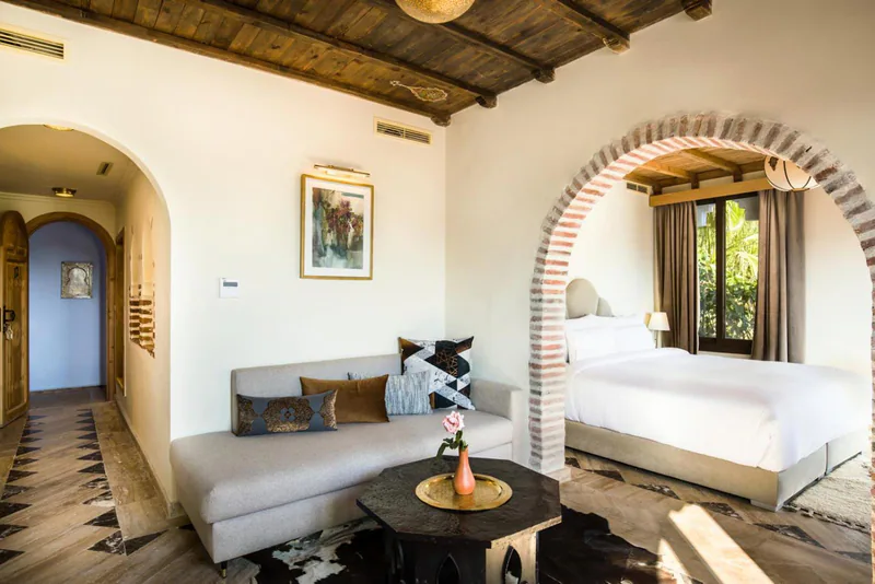 A suite sitting area with a low table and cushions, opening through an arch to the bedroom